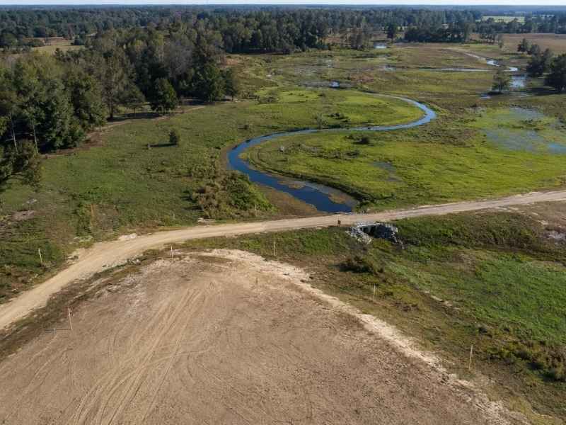 Flood study Raleigh North Carolina - Raleigh Civil Engineering Aerial view of a winding blue stream through green marshland, with a dirt road crossing the foreground.